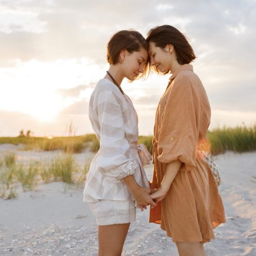 Two women  standing face to fase on beach near sea when sunset in evening Lifestyle lesbian couple travel on beach .